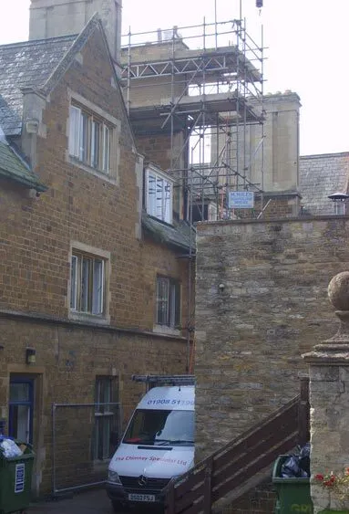 Scaffolding around the chimneys of a large stone building, with our van parked below