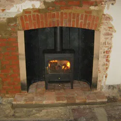 Wood burning stove in a restored brick fireplace with an arched opening