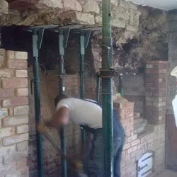 Builder working inside an inglenook fireplace supported by steel props