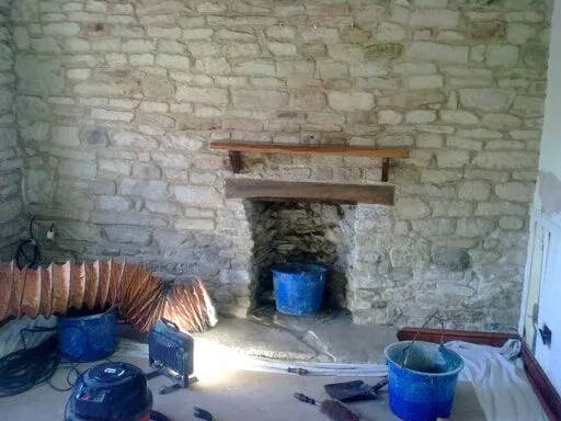 Fireplace opened up in a stone wall during a stove installation, with flue liner on the floor