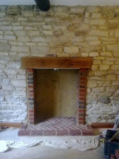 New brick fireplace opening with a timber beam and herringbone hearth