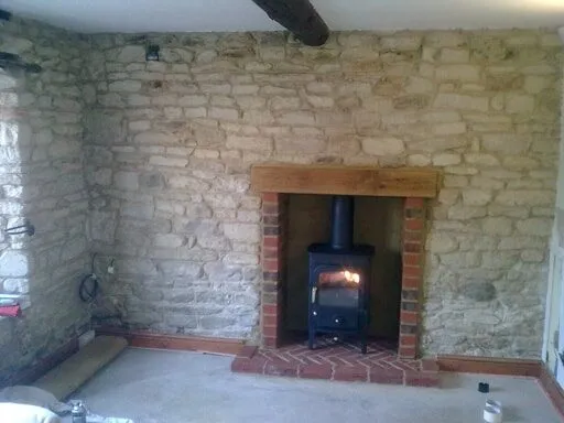 Lit wood burning stove in a brick fireplace set into a stone wall